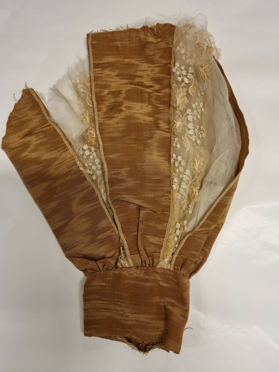 Kort erme med linning og god vidde. I silkerips og kniplinger. Organza fòr.
