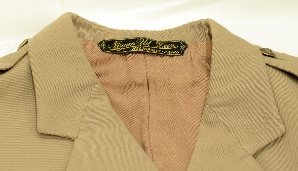 A.Uniformsjakke. Tropeuniform. Beige jakke i syntetisk materiale med 4 lommer foran. 8 knapper med emblem, skulderklaffene med rødt merke uten distinksjoner. Påsydd flygersymbolmerke foran. Jakken har fôr i armene og ved nakkepartiet. Belte med beltespenne.

B. Uniformslue. Luen har en brett festet med trykk-knapp på begge sider. Denne bretten kan brettes ut, og det blir en lue som kan festes under haken med to små knapper med emblem. Innvendig er det svettebånd og fôr.