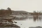 Fotografi från expedition till Grönland. Motiv av liten fiskeby belägen vid havsstranden. På stranden syns två mindre träbåtar.