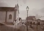 Fotografi från första svenska Antarktisexpeditionen 1901-1904. Motiv av man utanför liten kyrka i en stad eller by.