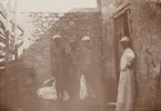 Fotografi från första svenska Antarktisexpeditionen 1901-1904. Motiv av tre nakna kvinnor vid en stenvägg.