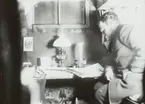 Fotografi från första svenska Antarktisexpeditionen 1901-1904. Motiv av man som sitter och läser inomhus vid fotogenlampa.