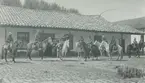 Fotografi från expedition till Peru 1920. Motiv av expeditionsdeltagare till häst utanför ett vitmålat hus.