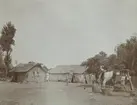Fotografi från expedition till Peru 1920. Motiv av två stenhus med halmtak och gård med vattenbrunn.