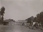 Fotografi från expedition till Peru 1920. Motiv av två stenhus med halmtak och en vattenbrunn.