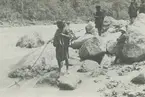 Fotografi från expedition till Peru 1920. Motiv av expeditionsdeltagare som sitter på klippor vid en flod i djungeln.