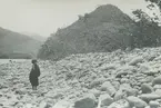 Fotografi från expedition till Peru 1920. Motiv av barn på stenig strand nedanför berg i djungeln.