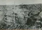 Fotografi från expedition till Östgrönland 1929. Dansk-svensk expedition under ledning av Lauge Koch. Svenska deltagare: Oscar Kulling och Helge Backlund. Motiv av stenig klippa med måttstock som visar klippans höjd.