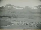 Fotografi från expedition till Östgrönland 1929. Dansk-svensk expedition under ledning av Lauge Koch. Svenska deltagare: Oscar Kulling och Helge Backlund. Vy över bosättning vid vatten nedanför ett stort berg.