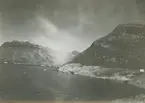 Fotografi från expedition till Östgrönland 1929. Dansk-svensk expedition under ledning av Lauge Koch. Svenska deltagare: Oscar Kulling och Helge Backlund. Vy över hav, snötäckta berg och molnprydd himmel.