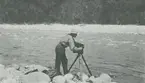 Fotografi från expedition till Peru 1920. Motiv av expeditionsdeltagare med kamera på flodstrand i djungeln.