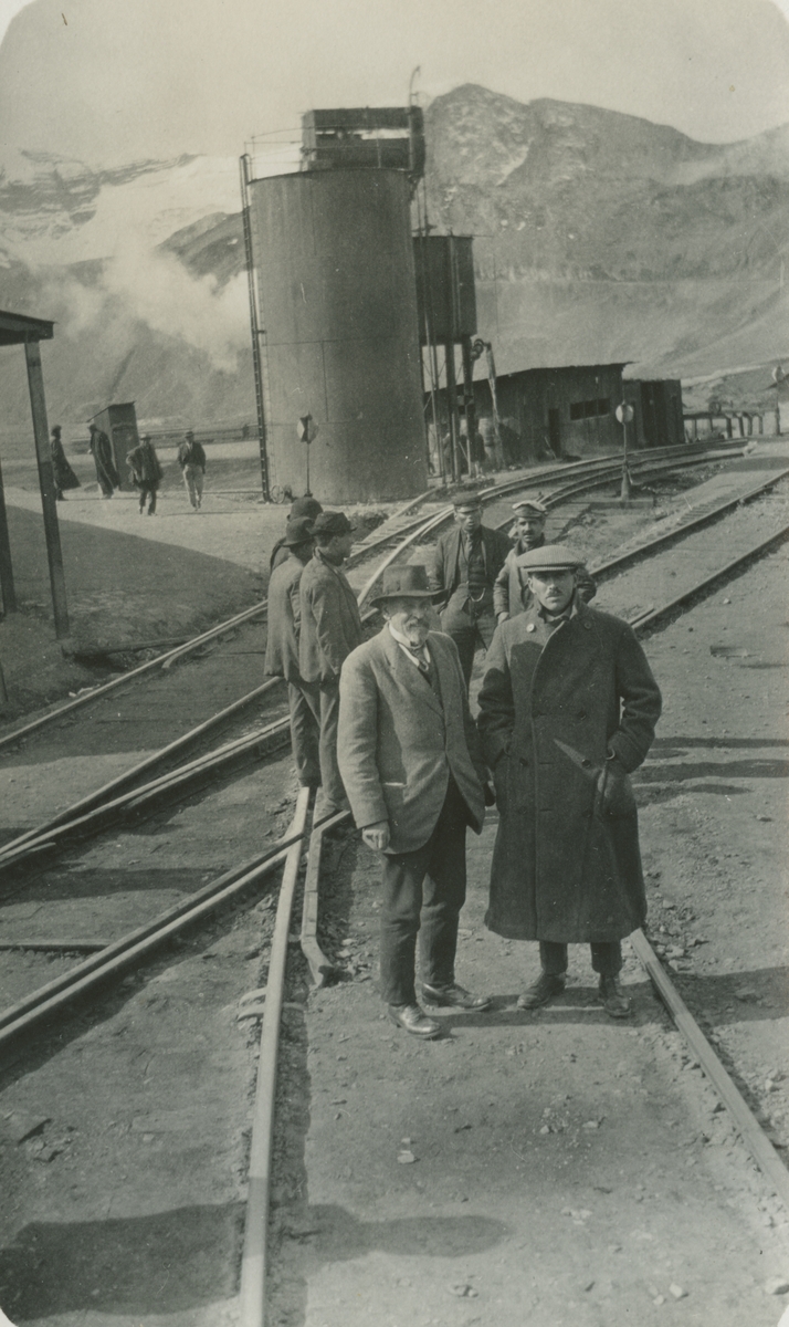 Fotografi från expedition till Peru 1920. Motiv av Otto Nordenskjöld med kollega som står framför järnvägsspår och vattencistern i ett bergslandskap.