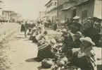 Fotografi från expedition till Peru 1920. Motiv av människor som säljer diverse varor på en gata i en stad/by.