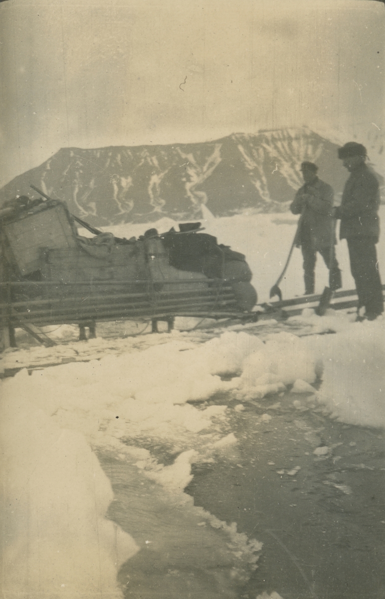 Fotografi från expedition till Spetsbergen. Motiv av expeditionsdeltagare som står med packning i snön nedanför berg.