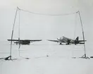 Fotografi från låda märkt Bernt Balchen. Balchen var norsk-amerikansk flygare, polarforskare och militär. Motiv av ett flygplan av typ Doublas DC-3 från United States Air Airforce med medar och ett glidflygplan på marken i ett snölandskap.