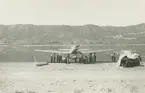 Fotografi från låda märkt Bernt Balchen. Balchen var norsk-amerikansk flygare, polarforskare och militär. Motiv av människor och flybåt på strand vid hav och berg.