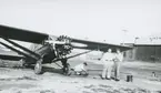 Fotografi från låda märkt Bernt Balchen. Balchen var norsk-amerikansk flygare, polarforskare och militär. Motiv av tre män som står på startbana vid ett flygplan. Mannen längst till höger är troligen Bernt Balchen.