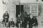 Fotografi från låda märkt Bernt Balchen. Balchen var norsk-amerikansk flygare, polarforskare och militär. Motiv av sex män som sitter utanför liten träbyggnad i Ontario, 1927.