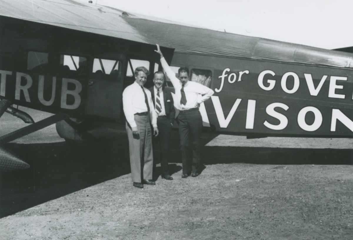 Fotografi från låda märkt Bernt Balchen. Balchen var norsk-amerikansk flygare, polarforskare och militär. Motiv av Balchen (längst till vänster) och två män vid flygplan med texten: "Trubee Davison for Governor".