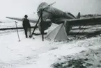 Fotografi från låda märkt Bernt Balchen. Balchen var norsk-amerikansk flygare, polarforskare och militär. Motiv av man vid flygplan i ett snötäckt landskap.