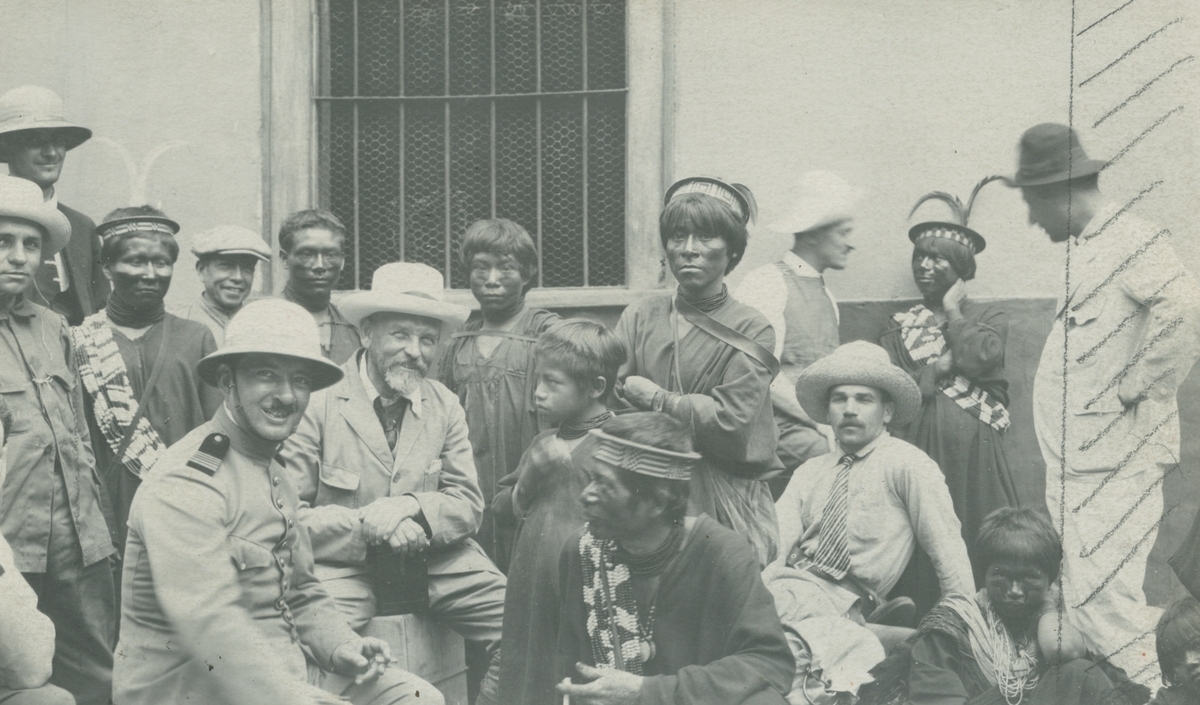 Fotografi från Peruexpedition 1920. Motiv av ett antal expeditionsmedlemmar och ursprungsfolk poserar tillsammans framför ett hus. Mannen med hatt och skägg i mitten av bilden är Otto Nordenskjöld.