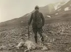 Fotografi från expedition till Sveagruvan. Motiv av man med pipa och gevär som poserar vid död ren.