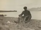 Fotografi från expedition till Sveagruvan. Motiv av man som sitter på stenig strand och leker med liten hund.