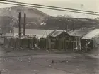 Bild från expedition i Antarktisområdet. Motiv av små träbyggnader och tunnor nedanför berg, 1933.