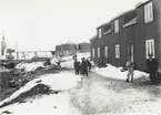 Bild från expedition i Antarktisområdet. Motiv av ett antal män på snöig gata utanför hus.