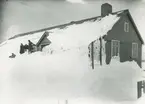 Bild från expedition i Antarktisområdet. Motiv av fyra personer vid ett insnöat hus.