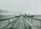 Fotografi från Spetsbergen. Motiv av brygga med räls vid havet.