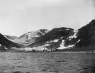 Fotografi från Grönland. Vy över hav, berg och strand med hus.