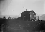 Fotografi från undsättningsexpeditionen med fartyget Uruguay 1903.. Motiv av man med hundar utanför litet trähus.
