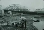 Fotografi från expedition till Spetsbergen. Motiv av man som tvättar kläder på strand i ett bergslandskap.