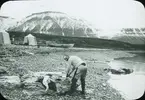 Fotografi från expedition till Spetsbergen. Motiv av man som tvättar kläder på strand i ett bergslandskap.