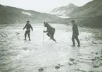 Fotografi från expedition till Spetsbergen. Motiv av tre män som försöker ta sig över vattendrag.