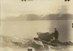 Fotografi från expedition till Spetsbergen 1920. Motiv av man med liten båt på strand vid vatten.