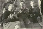 Fotografi från expedition till Spetsbergen 1920. Motiv av fyra män som sitter på trappa och håller i hundvalpar.