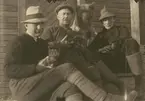 Fotografi från expedition till Spetsbergen 1920. Motiv av tre män och hudn som sitter på trappa. Männen håller i hundvalpar.
