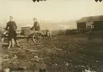 Fotografi från expedition till Spetsbergen 1920. Motiv av två män vid en träkärra framför ett hus.