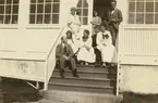 Fotografi från Albin Ahrenbergs resa till Grönland 1929. Motiv av en grupp män och kvinnor som sitter på en hustrappa.