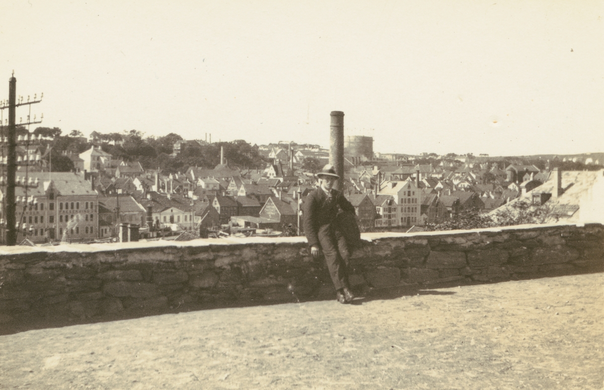 Fotografi från Albin Ahrenbergs resa till Grönland 1929. Motiv av man som sitter och vilar på stenmur i stad.