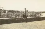 Fotografi från Albin Ahrenbergs resa till Grönland 1929. Motiv av man som sitter och vilar på stenmur i stad.