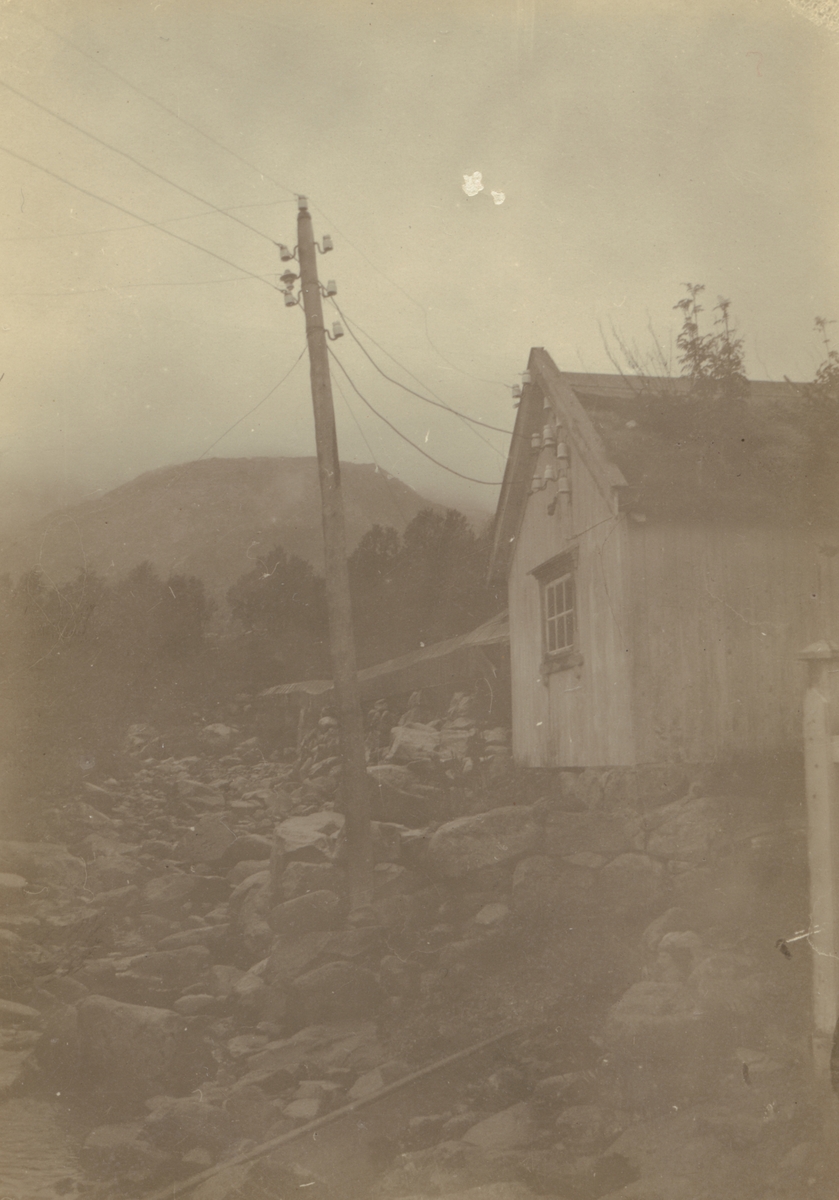 Fotografi från Albin Ahrenbergs resa till Grönland 1929. Motiv av hus och telefonstolpe i stenigt bergslandskap.