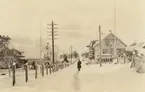 Fotografi från Albin Ahrenbergs resa till Grönland 1929. Motiv av telefonstolpar och man på snötäckt gata i liten stad.