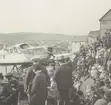 Fotografi från Albin Ahrenbergs resa till Grönland 1929. Motiv av en stor samling människor vid flygbåt i stad.