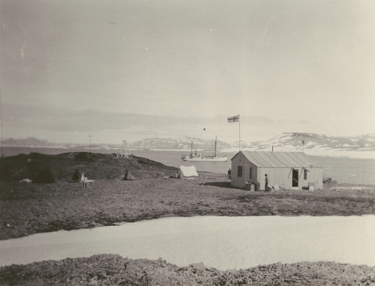 Fotografi från Ahlmannexpeditionen 1931. Motiv av litet trähus och tält.