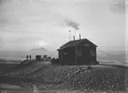 Fotografi från undsättningsexpeditionen med fartyget Uruguay 1903. Motiv av män vid hus i islandskap.