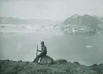 Fotografi från expedition till Spetsbergen. Motiv av kvinna som sitter på sten vid strand.