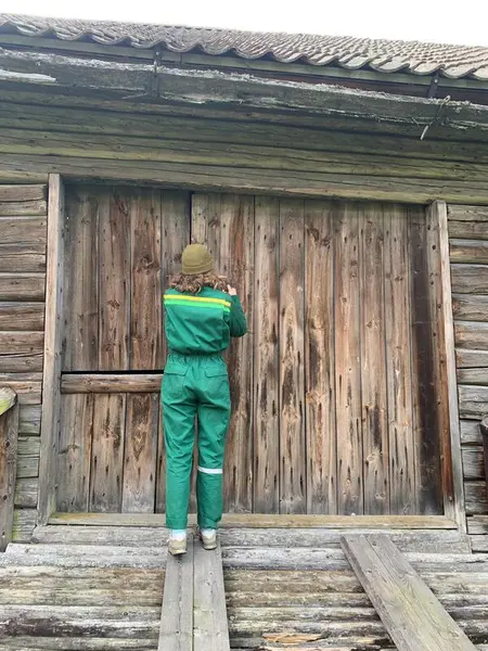 Bildet viser ei ung kvinne som låser en låvedør. Hun har på seg en heldress.